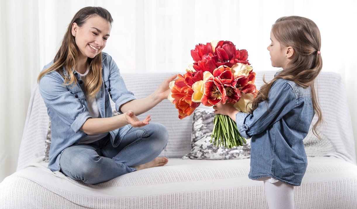 Happy mother's Day. Little sweet daughter with a large bouquet of tulips congratulates her mother. In the interior of the living room, the concept of a happy family life